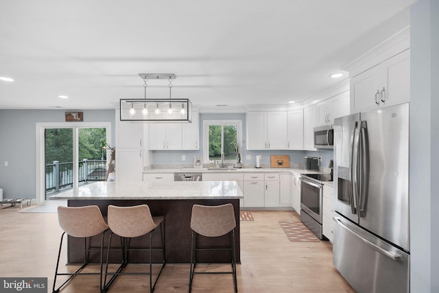 kitchen with stainless steel appliances, a kitchen island, a breakfast bar, white cabinetry, and light wood-type flooring