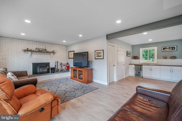 living area featuring wine cooler, a wood stove, light wood-style floors, recessed lighting, and brick wall