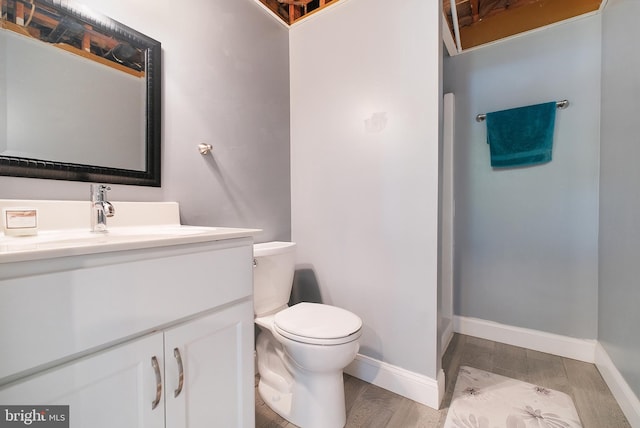 bathroom with toilet, wood finished floors, vanity, and baseboards