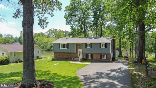 raised ranch with brick siding, driveway, a front yard, and central AC