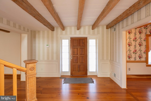 foyer with beamed ceiling, wallpapered walls, and wood finished floors