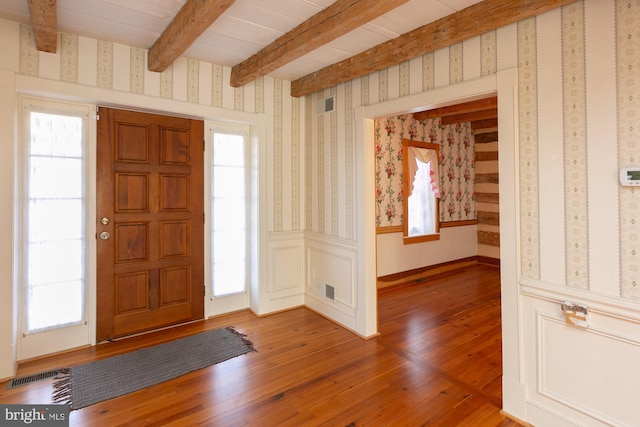 foyer entrance with visible vents, beam ceiling, and light wood-type flooring