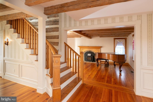stairway with beamed ceiling, hardwood / wood-style flooring, and wallpapered walls