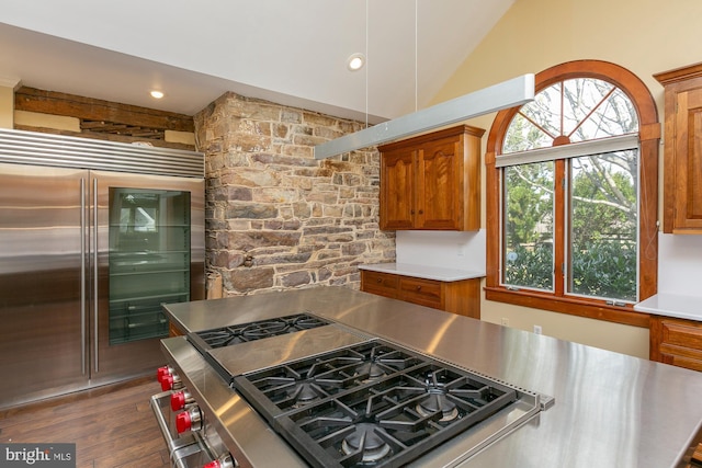 kitchen with lofted ceiling, dark wood-type flooring, brown cabinets, built in fridge, and stovetop with downdraft