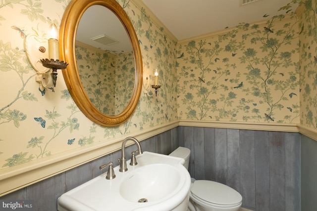 half bathroom with visible vents, a sink, wainscoting, and wallpapered walls