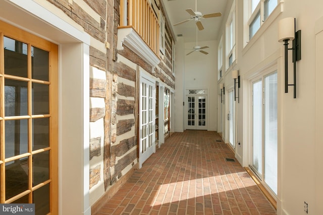 hall with a high ceiling, a healthy amount of sunlight, french doors, and brick floor