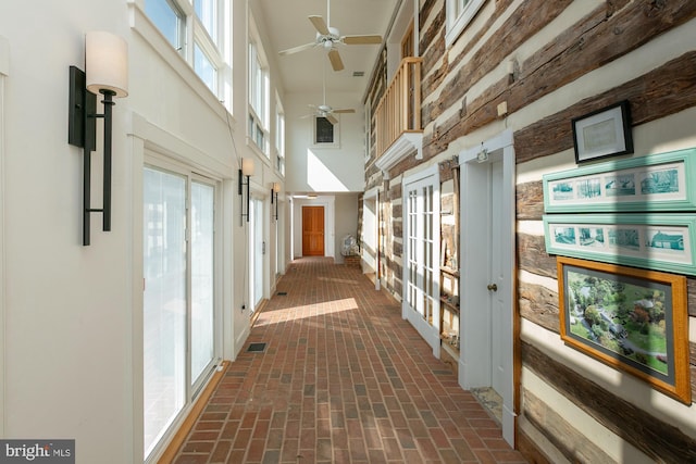 hallway with a wealth of natural light, brick floor, and a towering ceiling