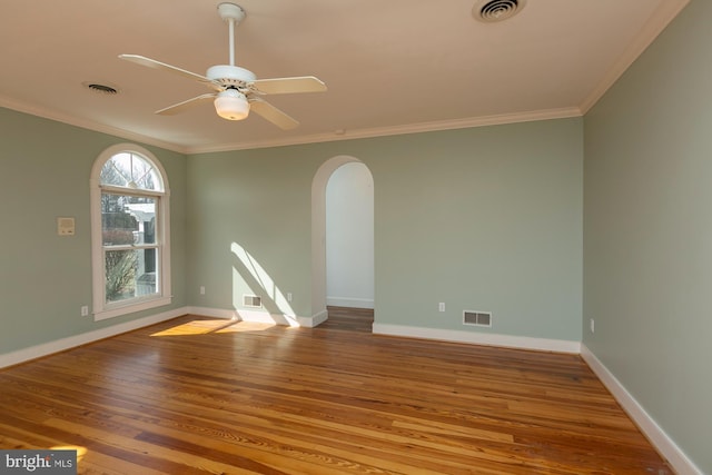 spare room with arched walkways, visible vents, ornamental molding, and wood finished floors