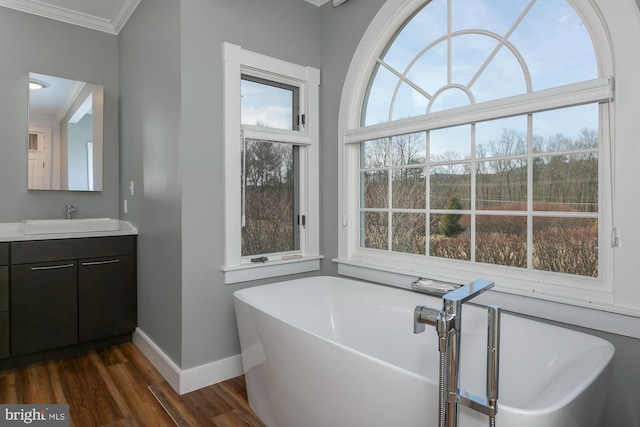 full bath featuring a freestanding bath, baseboards, ornamental molding, and wood finished floors