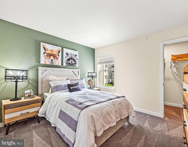 carpeted bedroom featuring a walk in closet and baseboards