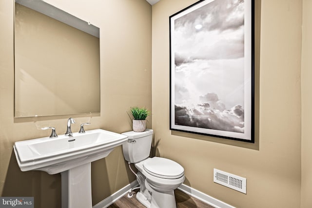 bathroom featuring visible vents, baseboards, toilet, wood finished floors, and a sink