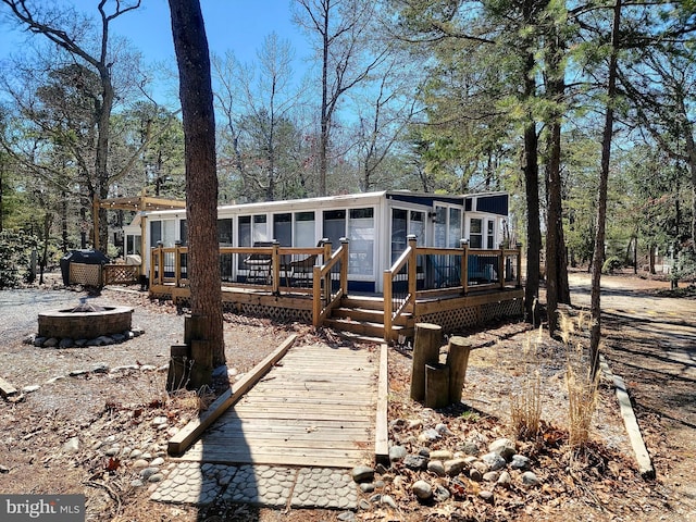 rear view of property featuring a fire pit, a wooden deck, and a sunroom