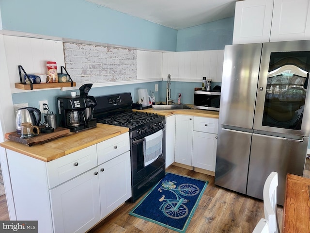 kitchen featuring white cabinets, a sink, appliances with stainless steel finishes, butcher block counters, and wood finished floors