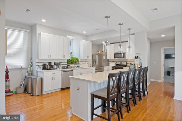 kitchen with visible vents, a breakfast bar, light wood-style floors, white cabinetry, and stainless steel appliances