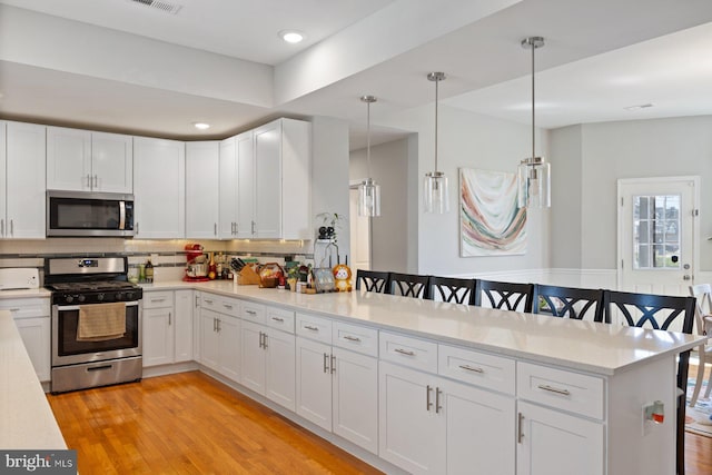 kitchen featuring stainless steel appliances, a peninsula, light wood-style floors, and white cabinetry
