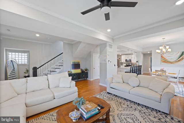 living area with crown molding, wood finished floors, ceiling fan with notable chandelier, and stairs