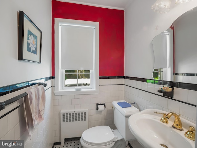 half bathroom featuring wainscoting, a sink, toilet, radiator, and tile walls