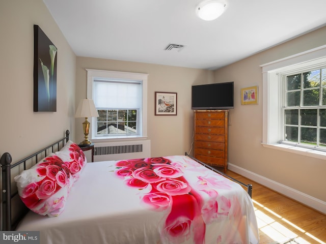 bedroom featuring visible vents, baseboards, radiator, and wood finished floors
