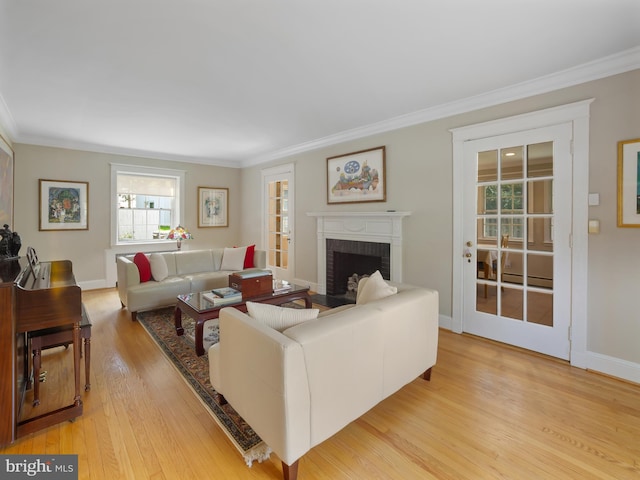 living room featuring a brick fireplace, baseboards, ornamental molding, and light wood-type flooring