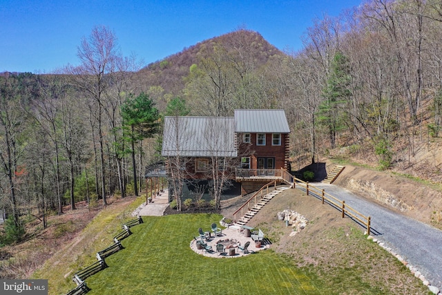 back of property featuring driveway, stairs, log exterior, a yard, and metal roof
