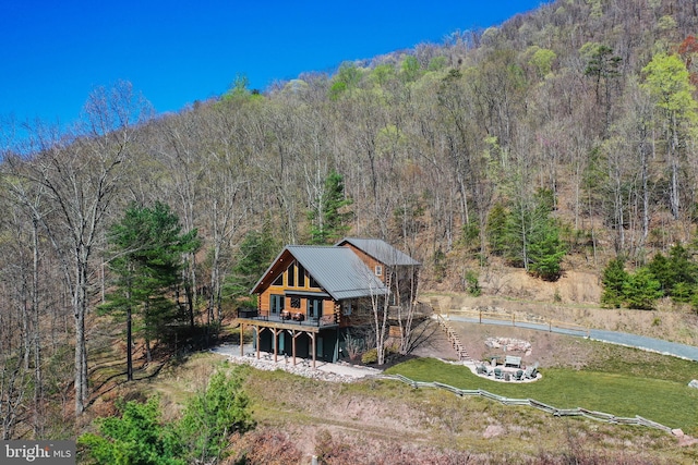 back of property with a view of trees, a wooden deck, and metal roof
