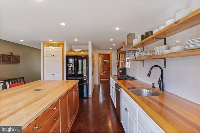 kitchen with open shelves, a sink, wall chimney range hood, wooden counters, and stainless steel appliances