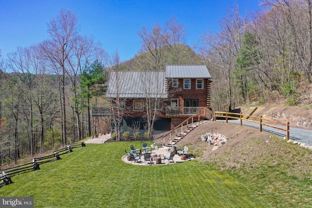 back of property featuring log siding, stairway, an outdoor fire pit, metal roof, and a lawn