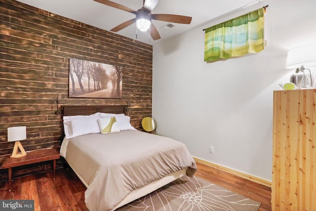 bedroom featuring baseboards, wooden walls, visible vents, ceiling fan, and wood finished floors