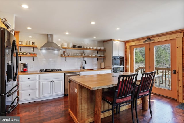 kitchen featuring wood counters, wall chimney exhaust hood, black appliances, and open shelves