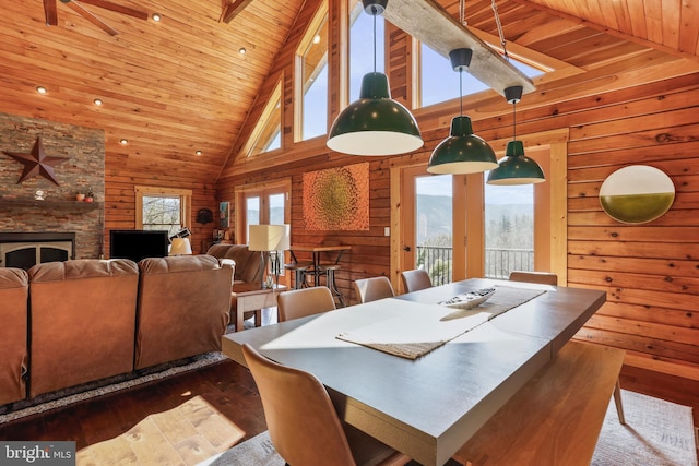 dining area featuring wooden ceiling, hardwood / wood-style flooring, a fireplace, wood walls, and high vaulted ceiling