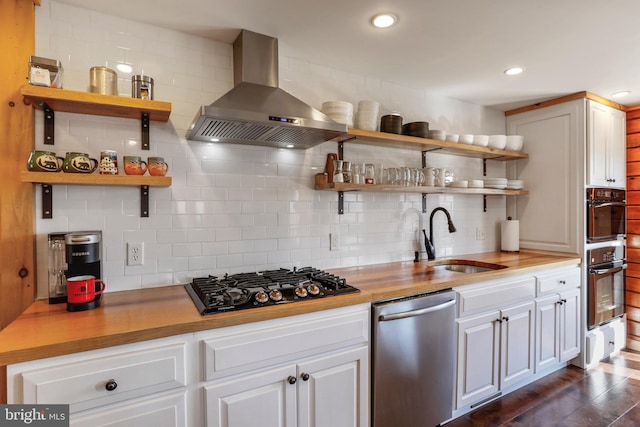 kitchen with wall chimney range hood, black gas cooktop, open shelves, stainless steel dishwasher, and a sink