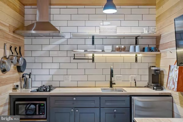 bar featuring tasteful backsplash, appliances with stainless steel finishes, a sink, and wall chimney range hood
