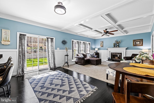 living area featuring a healthy amount of sunlight, a fireplace with raised hearth, a wainscoted wall, and coffered ceiling