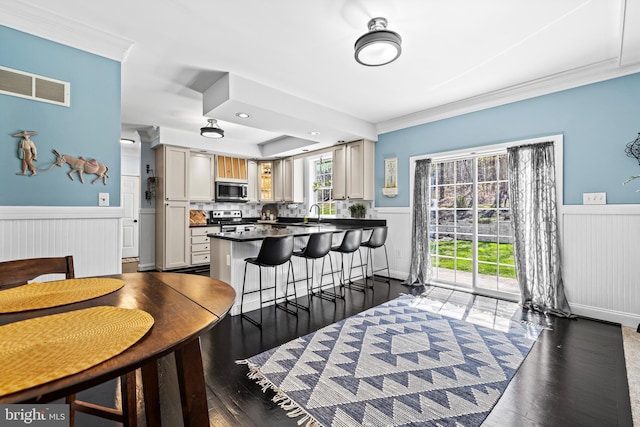 dining area featuring ornamental molding, visible vents, a wainscoted wall, and wood finished floors
