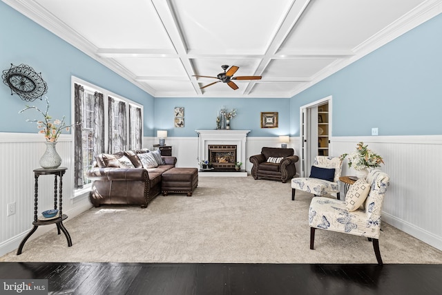living area with coffered ceiling, ceiling fan, wood-type flooring, and wainscoting