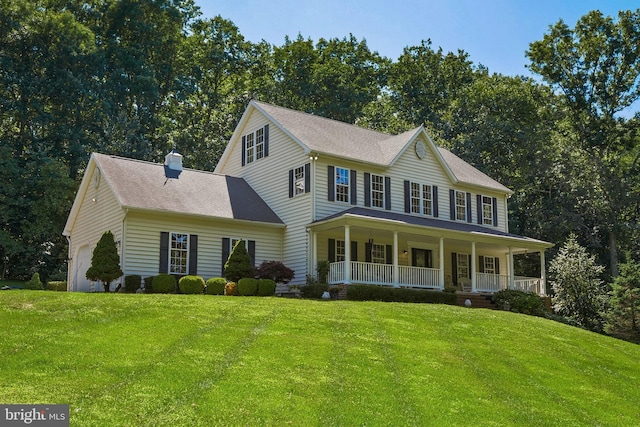 colonial inspired home with a chimney, covered porch, a front yard, and a garage