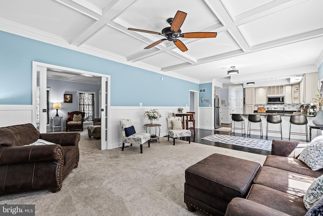 carpeted living area featuring ceiling fan, beamed ceiling, a wainscoted wall, and coffered ceiling