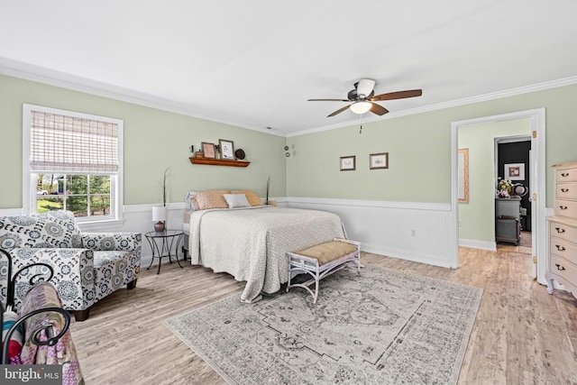 bedroom featuring light wood-style flooring, ceiling fan, crown molding, and wainscoting