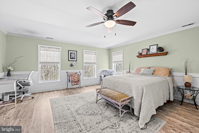 bedroom featuring crown molding, visible vents, a wainscoted wall, and wood finished floors