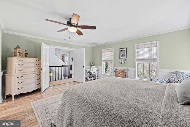 bedroom featuring wainscoting, wood finished floors, ceiling fan, and ornamental molding