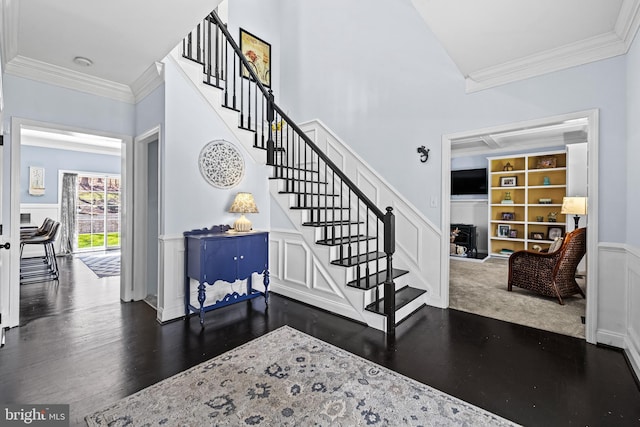 entryway featuring crown molding, a decorative wall, a wainscoted wall, stairway, and wood finished floors