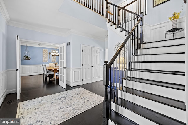 stairs featuring crown molding, a wainscoted wall, a decorative wall, and a chandelier
