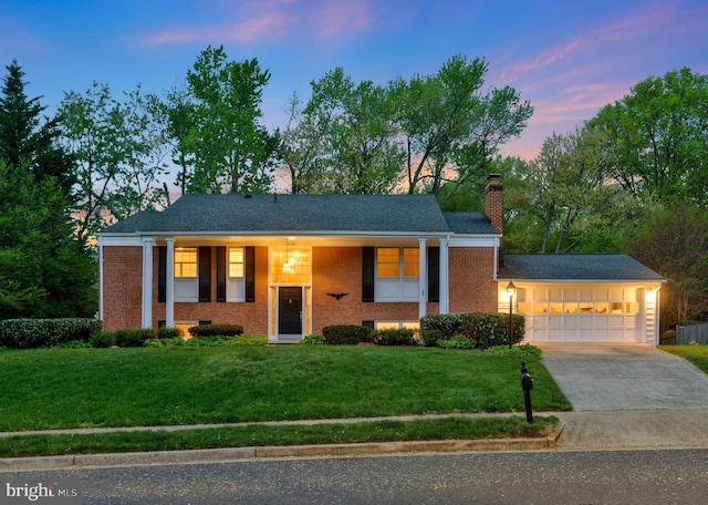 bi-level home with concrete driveway, a chimney, an attached garage, a yard, and brick siding