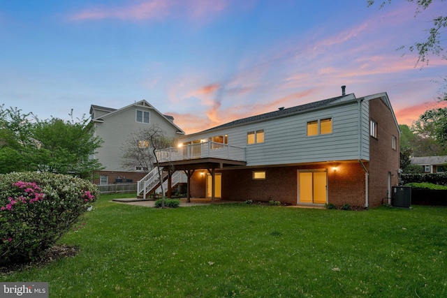 back of property at dusk with a deck, stairway, brick siding, and a lawn