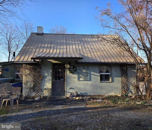 view of front facade featuring metal roof, stucco siding, and a chimney