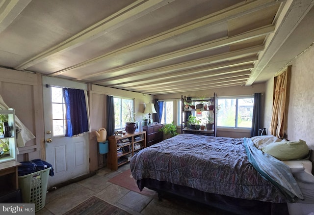 bedroom with stone tile floors, multiple windows, and beamed ceiling