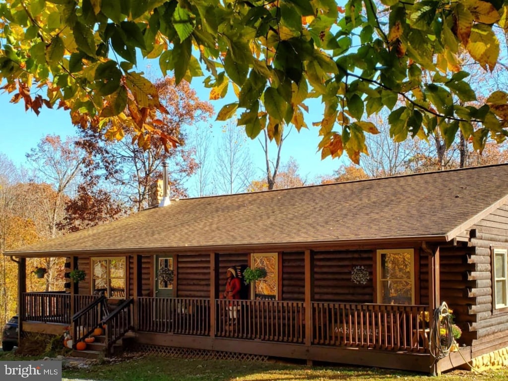 view of front of home with a porch, a shingled roof, and log exterior
