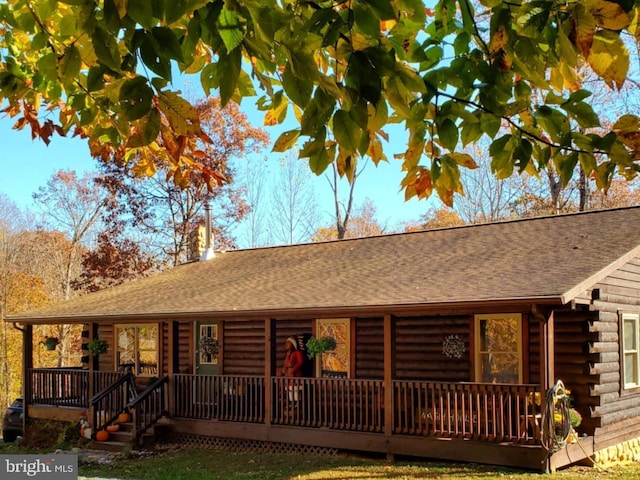 view of front of home with a porch, a shingled roof, and log exterior