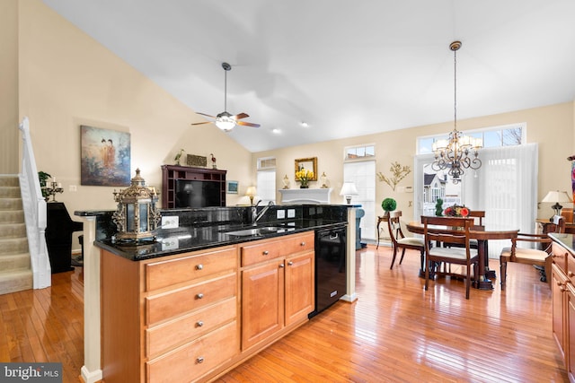 kitchen featuring vaulted ceiling, black dishwasher, light wood-style floors, ceiling fan with notable chandelier, and a sink