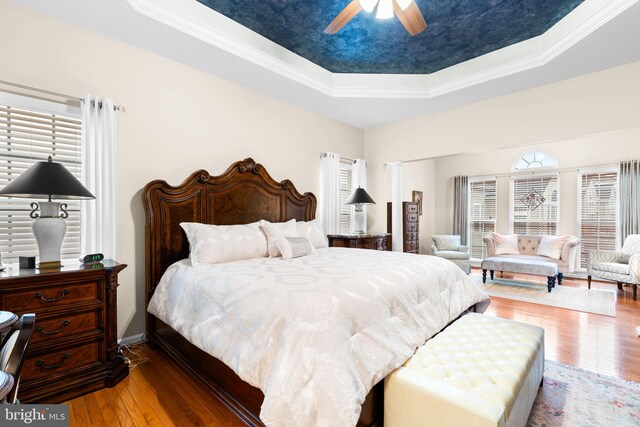 bedroom with baseboards, a raised ceiling, ceiling fan, crown molding, and hardwood / wood-style floors